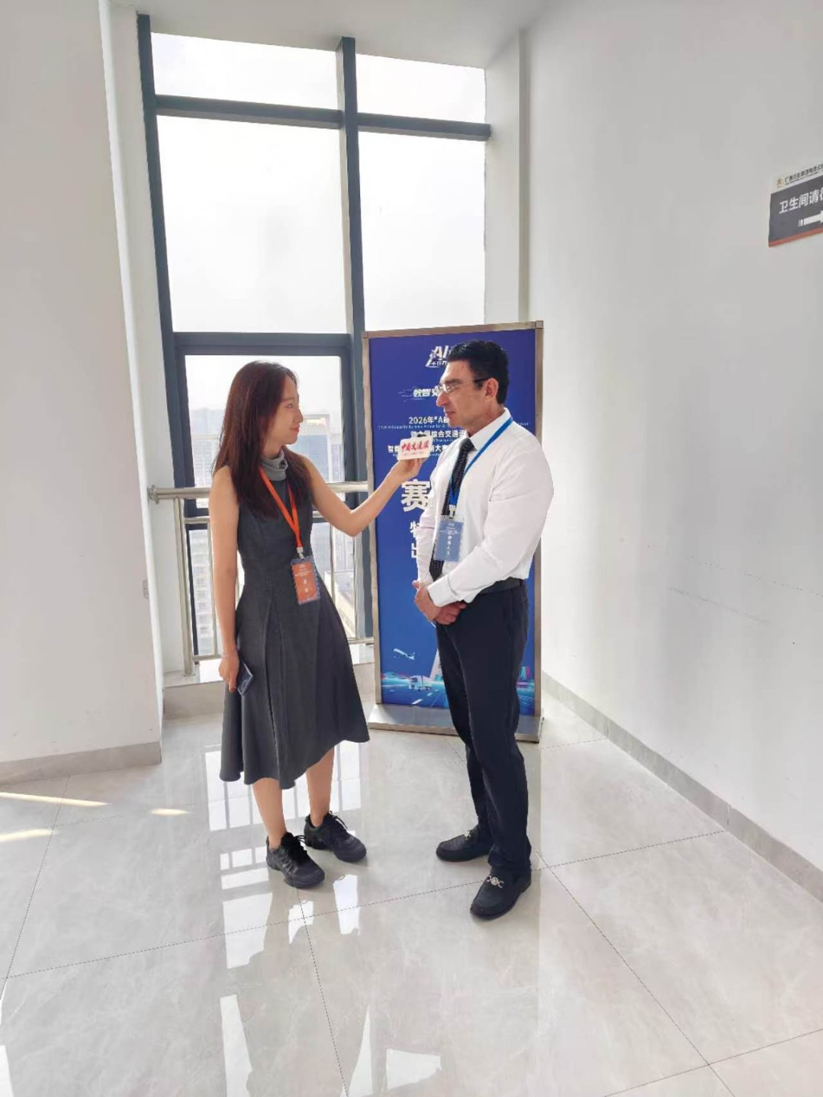 Dr David Vainer answering a journalist's questions beside the Nanning finals event banner