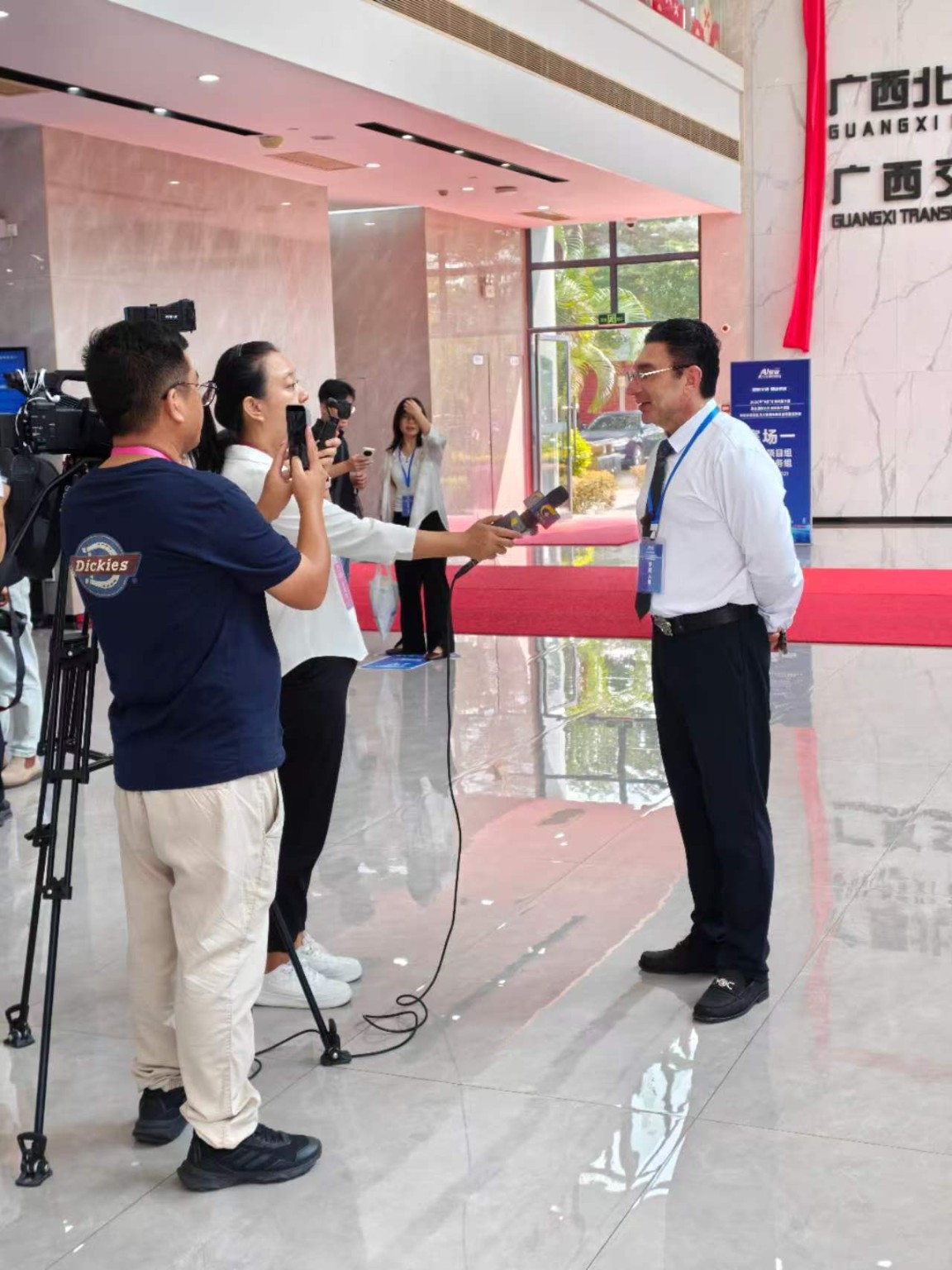 Dr David Vainer speaking with journalists and a television camera crew in the event lobby